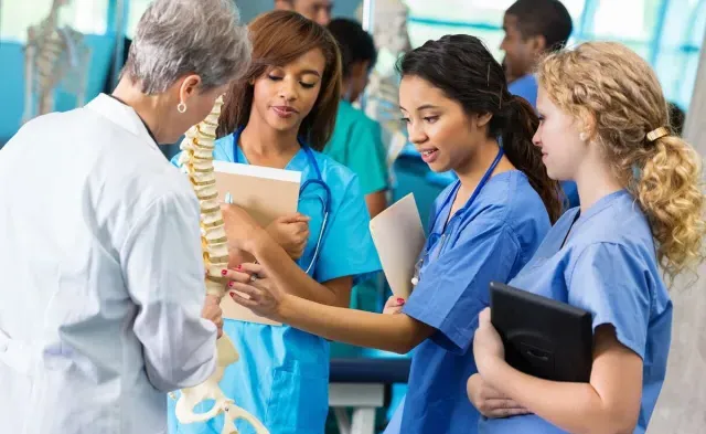 Three nursing students learning skeletal structure from nurse teacher